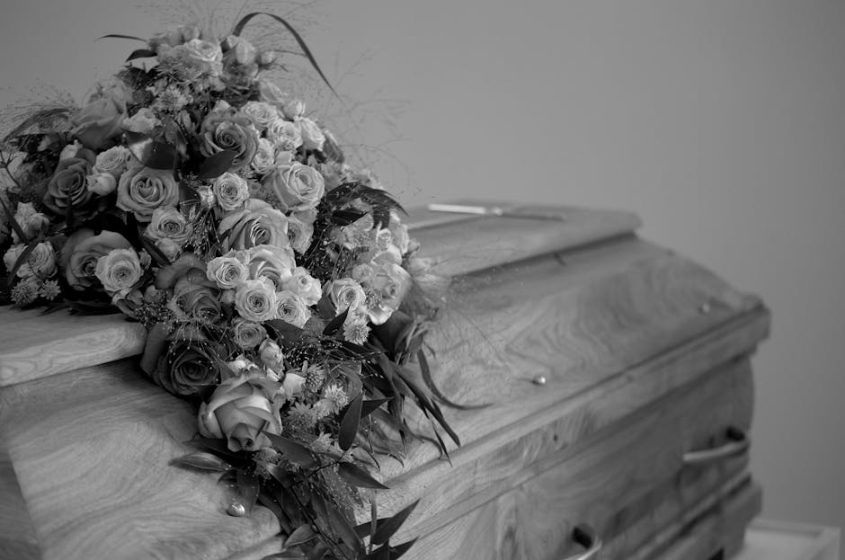 A large, elegant floral tribute featuring an arrangement of various roses, including both fully bloomed and budding roses, predominantly in shades of white and light pink, accented with darker foliage