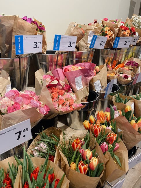A display of various flower bouquets arranged in metal buckets wrapped in brown kraft paper at Merton Florist, showcasing vibrant tulips in red, orange, and pink hues, with some bouquets featuring ros