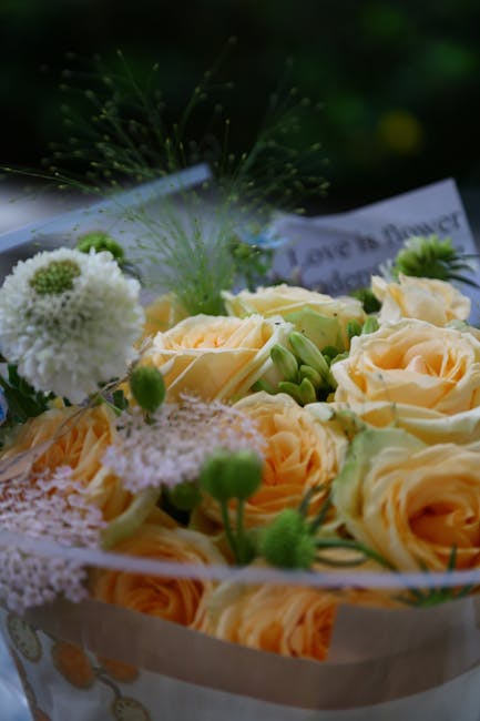A close-up of a floral arrangement featuring pale peach roses with softly curled petals, accompanied by small white and green blooms, and delicate greenery including fine, star-shaped foliage and gree